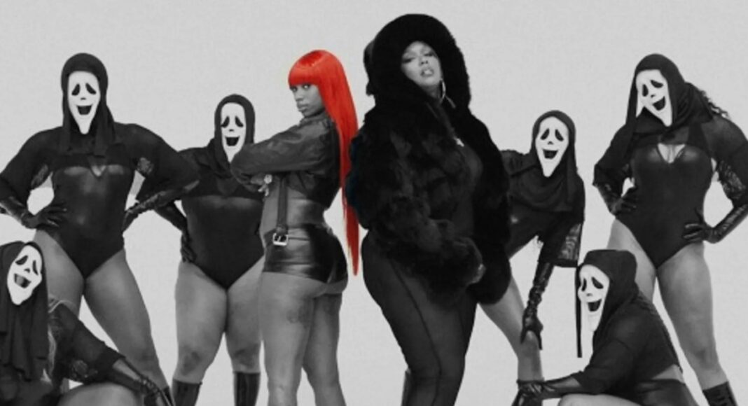 Group of dancers in black outfits and white ghost masks pose with a central figure featuring bright red hair in a studio setting.