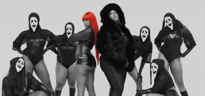 Group of dancers in black outfits and white ghost masks pose with a central figure featuring bright red hair in a studio setting.