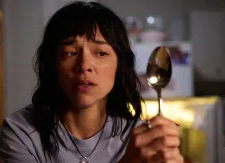 Woman in a kitchen holding a metal spoon, looking worried and distressed.