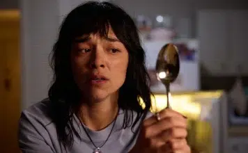 Woman in a kitchen holding a metal spoon, looking worried and distressed.