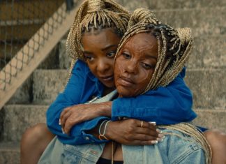 ‘Ardente Vingança’: THRILLER com Janelle Monáe ganha novo clipe arrepiante; Confira! Two women sit on concrete stairs, embracing in a comforting hug, wearing blue jackets and denim.