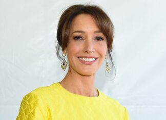 Smiling woman with brown hair wearing a bright yellow textured dress and gold dangling earrings, posing for a portrait.
