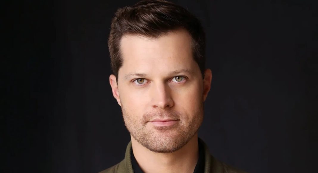 Close-up portrait of a man with short dark hair and light stubble against a dark backdrop