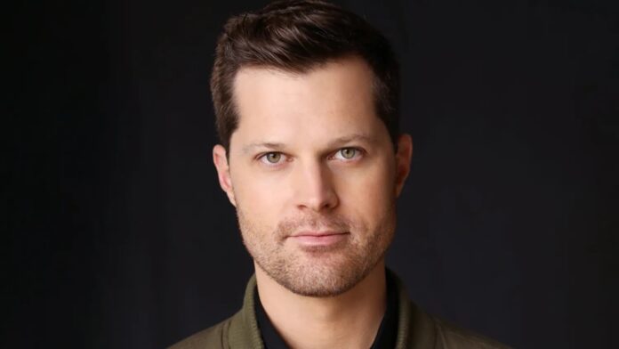 Close-up portrait of a man with short dark hair and light stubble against a dark backdrop