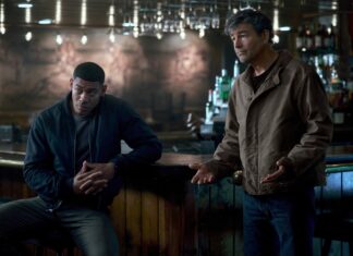 ‘Lanternas’: Série do DCU é ACLAMADA pela crítica internacional; Confira! Two men talk at a dimly lit bar; one sits leaning on the counter, the other stands with open hands gesturing.