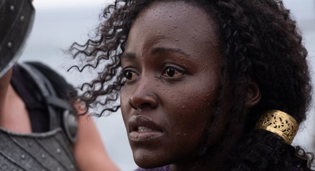 Close-up of a dark-skinned woman with wet skin and curly hair, looking distressed at a figure in armor to her left, wearing a gold hair cuff.