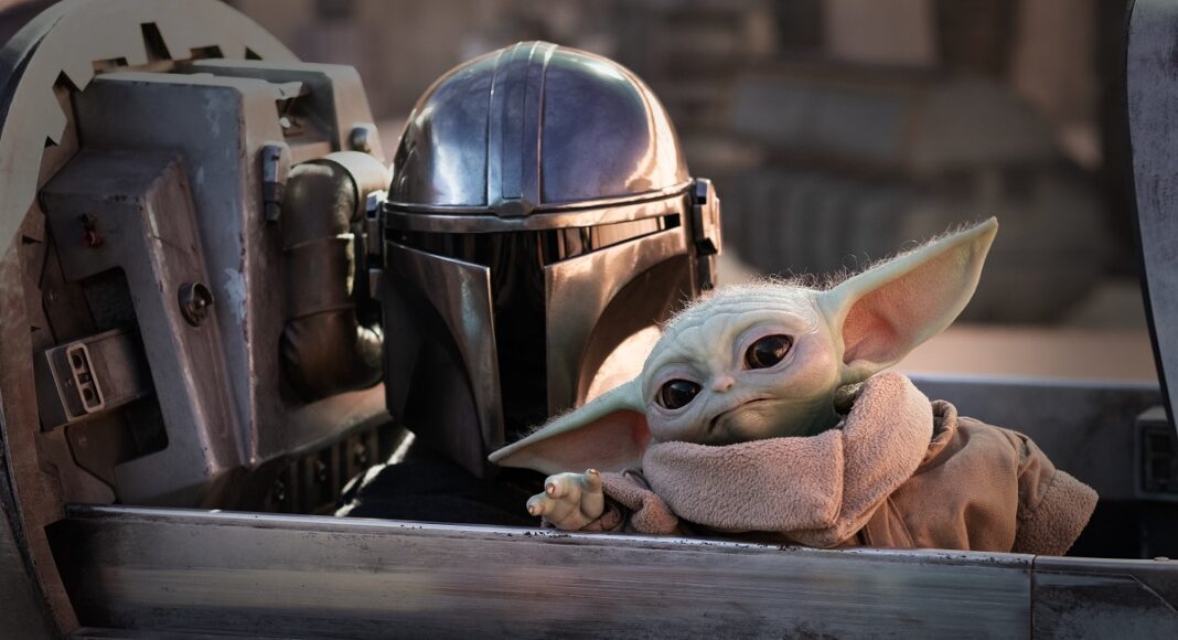 Mandalorian helmeted figure with Grogu (Baby Yoda) leaning forward inside a starship cockpit,
