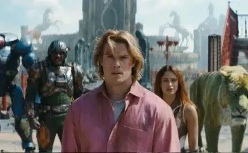 Film still: a man in a pink shirt leads a diverse group through a bustling fantasy city with a tiger nearby. (Note: concise summary focusing on the scene and characters.)