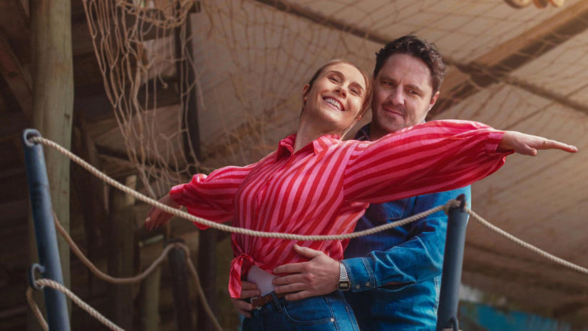 Smiling couple dancing with arms outstretched; man stands behind, supporting the woman’s waist in a striped red blouse.
