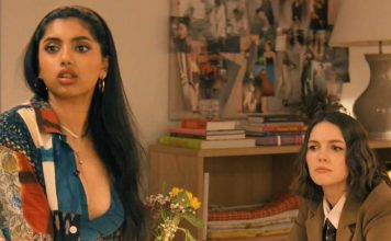 Two women in a living room: one with long dark hair in a colorful patchwork shirt speaks, the other in a brown blazer listens nearby.