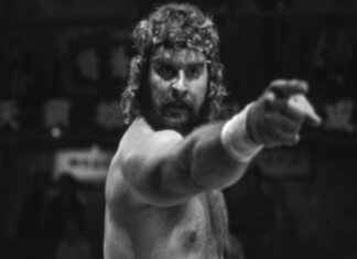 Donald Gibb, astro de ‘A Vingança dos Nerds’, falece aos 71 anos Bearded, shirtless wrestler with long hair points toward the camera in a black-and-white scene.