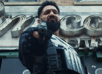 Jon Bernthal explica por que inicialmente recusou interpretar o Justiceiro em ‘Demolidor: Renascido’ A rugged man in tactical gear points a pistol at the camera, in a gritty urban setting with metallic signage behind him.