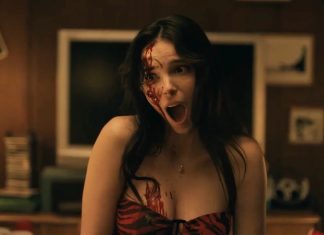 Woman with blood on her face and chest, mouth open in a scream in a dimly lit room.
