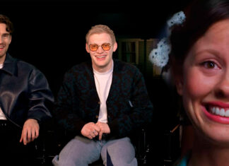 Three people in a dark studio: two men on the left, one wearing a leather jacket and the other with orange-tinted glasses, and a large, smiling woman’s close-up on the right.