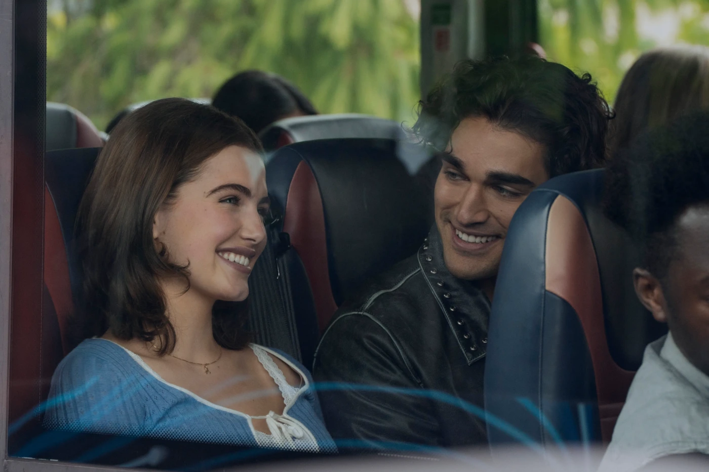 Two young people on a bus smiling at each other and enjoying a conversation.