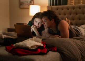Couple lying on a bed in a dimly lit room, looking at a laptop together men and women.