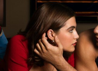 Man gently cups a woman's ear as they lean in and gaze at each other in a tender, intimate moment.
