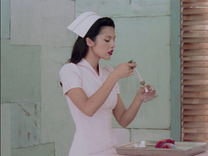 Young woman in a white nurse uniform and hat uses a dropper to transfer liquid into a small glass on a tray.