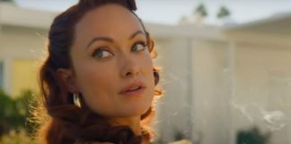 Close-up of a woman with wavy red hair looking over her shoulder in warm sunlight outdoors, wearing earrings.
