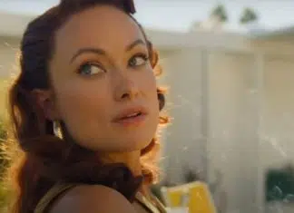 Close-up of a woman with wavy red hair looking over her shoulder in warm sunlight outdoors, wearing earrings.