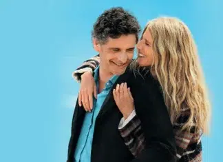 10 Dicas de Filmes que resolvem sua noite em poucas horas A couple is hugging and smiling at each other against a bright blue backdrop, showing warmth and affection.