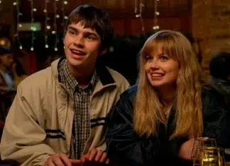 Two young adults smiles while leaning at a dimly lit bar with warm lights in the background, enjoying a night out.