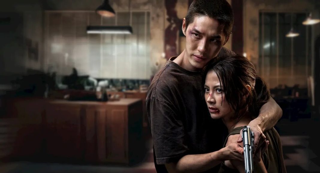 Man and woman in a dim kitchen; the man holds the woman, who grips a handgun and looks wary or scared.
