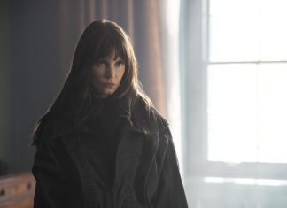 Sylvia Hoeks se junta ao elenco de ‘Disavowed’, novo thriller de ação da Apple TV Young woman with long brown hair wearing a black coat stands in a dim room, gaze focused off to the side by a bright window.