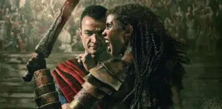 Two armored fighters collide in a dusty arena, one raising a bloodstained weapon as the crowd watches.