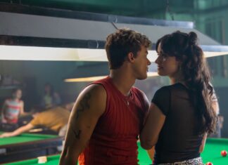 Couple leaning in for a kiss beside a pool table in a dim billiards hall.