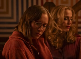 Crítica | ‘Acampamento Miasma: Adolescência, Sexo e Morte’ faz das franquias de TERROR uma autópsia cultural Two women sit side by side in a warm, dim room; the foreground woman wears glasses and an orange sweater.|Two women seated indoors with soft amber lighting, one in the foreground wearing glasses and a rust-colored sweater, looking down.|Contemplative scene of two women in a warmly lit room, with a geometric-patterned wall in the background.|Foreground: woman with glasses in an orange knit sweater; behind her, a blonde woman with curls in a red-toned setting.|Two thoughtful women in a cozy, amber-lit space, one in the foreground and the other slightly behind.