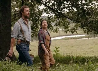 Matthew McConaughey solta a voz no novo clipe de ‘The Rivals of Amziah King’, seu primeiro filme em SEIS anos Two adults walking through a grassy rural area beside a tree, the man in a blue shirt with suspenders and the woman in overalls and a plaid shirt.