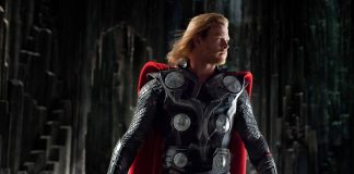 Thor in black armor and red cape stands in a dark cavernous setting, gripping Mjolnir in his left hand.