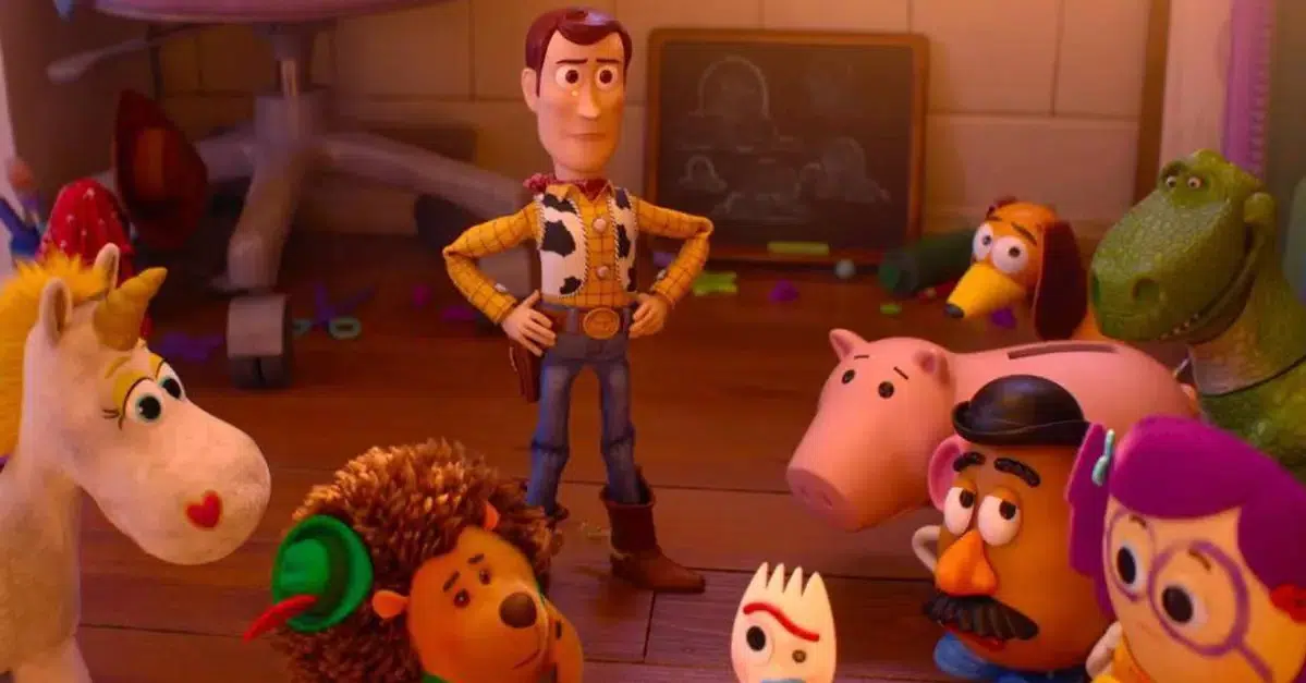 Woody stands with hands on hips among a circle of toy characters like a unicorn, hedgehog, pig, and dinosaur in a cluttered playroom.