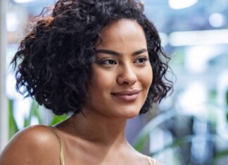 Portrait of a woman with short curly hair smiling softly in a bright indoor setting.