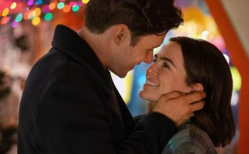 Couple smiling and embracing, head to head, with colorful festive lights in the background.
