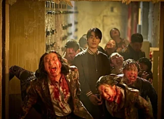 Young man in a black jacket stands calmly in a dim, blood-splattered hallway as snarling, zombified figures swarm around him.